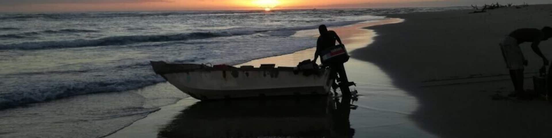 A sunset over a beach with a boat and a person on a bicycle.