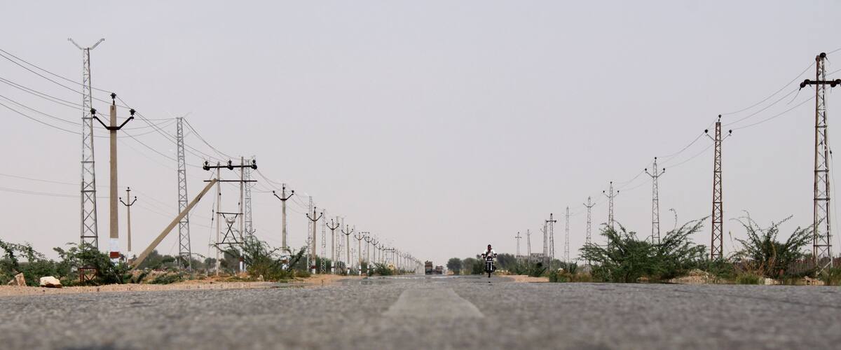 A long road flanked by power lines and sparse vegetation.