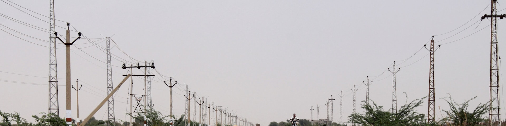 A long road flanked by power lines and sparse vegetation.