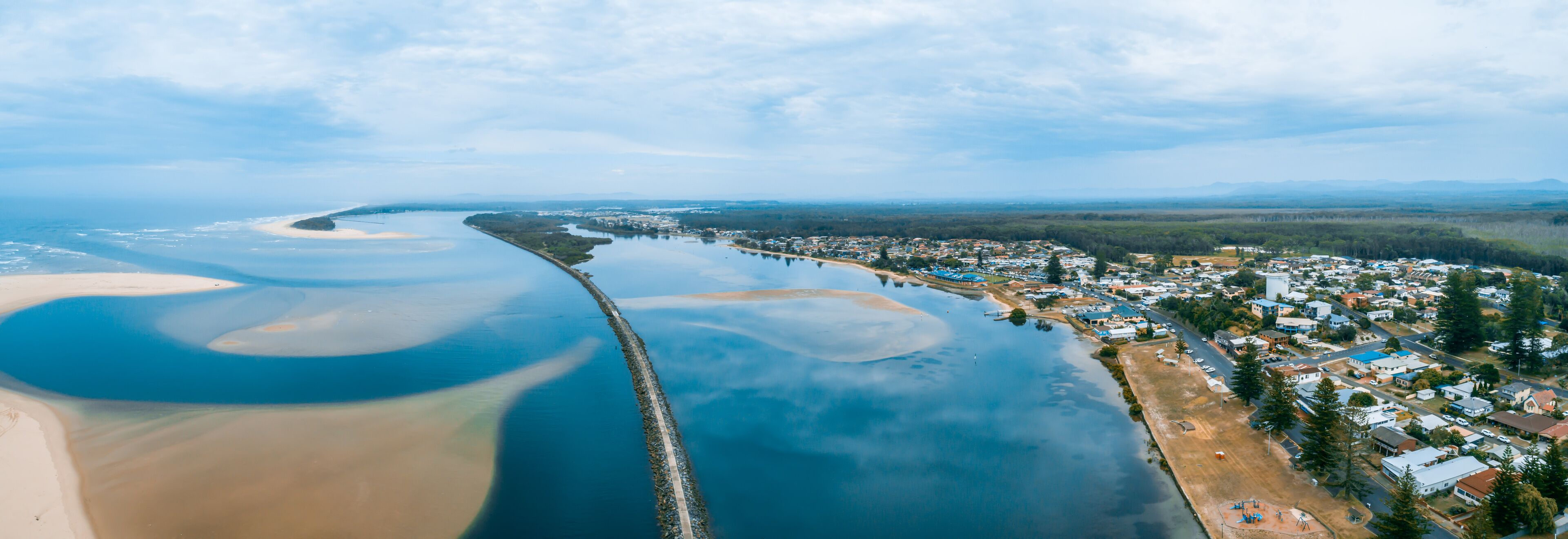 An aerial view of a coastal town with a beach, a pier, and a river.