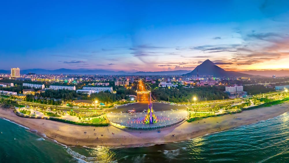 A coastal cityscape at sunset with a prominent mountain in the background.