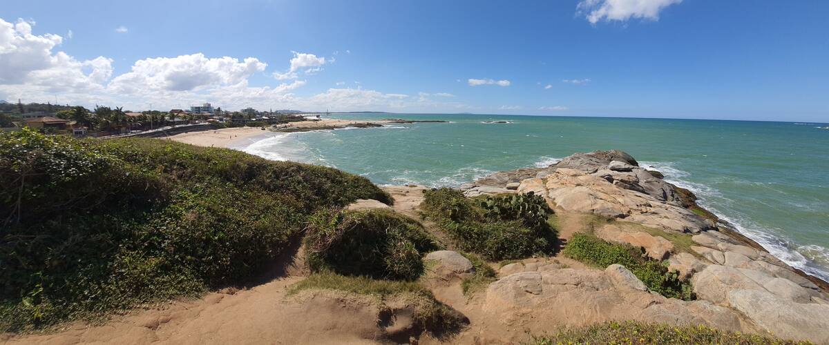 A coastal landscape with a sandy beach, rocky outcrops, and a clear blue sky.