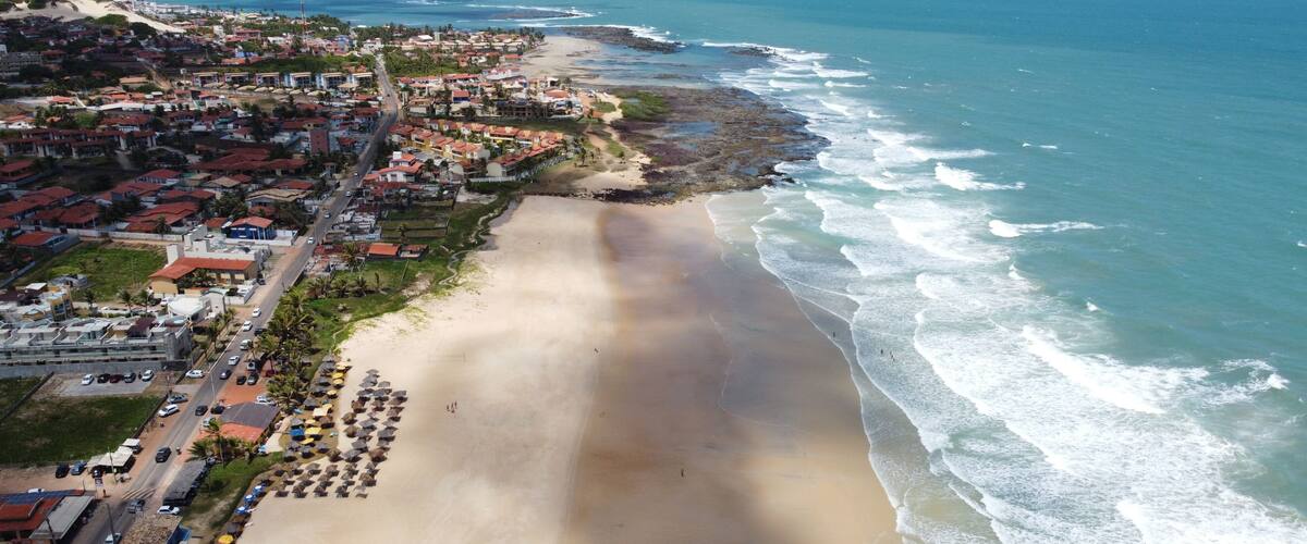 A coastal town with a wide sandy beach, a rocky shoreline, and residential buildings.