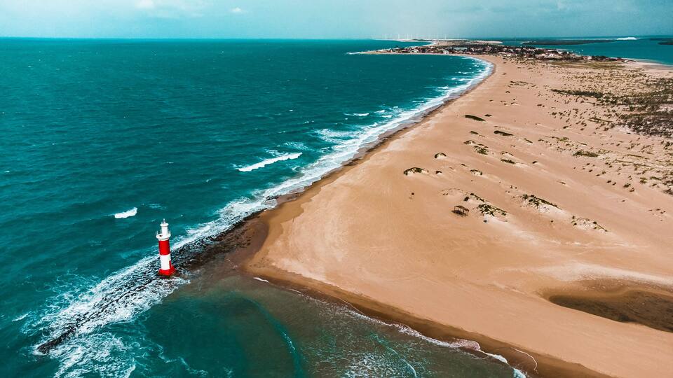 A coastal landscape with a lighthouse, sandy beach, and ocean waves.