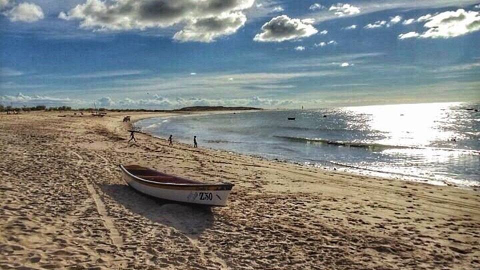 A sandy beach with a boat labeled "LAXO" and a clear sky with clouds.