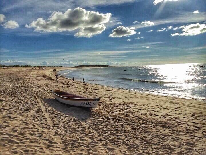 A sandy beach with a boat labeled "LAXO" and a clear sky with clouds.