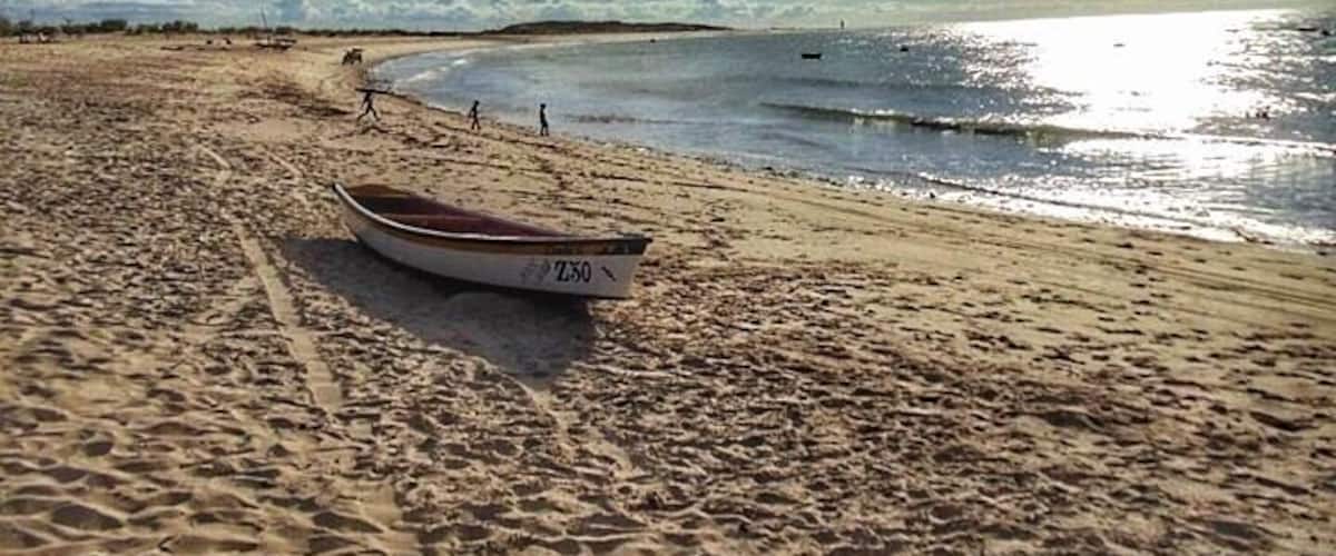 A sandy beach with a boat labeled "LAXO" and a clear sky with clouds.