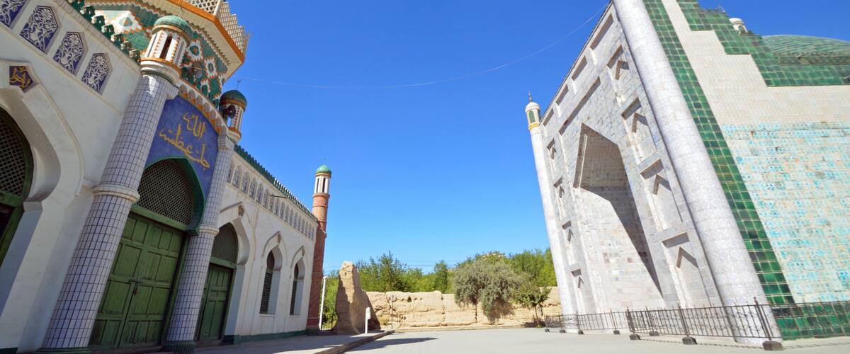 A mosque with a green dome and minarets, and a large white building with a green roof.
