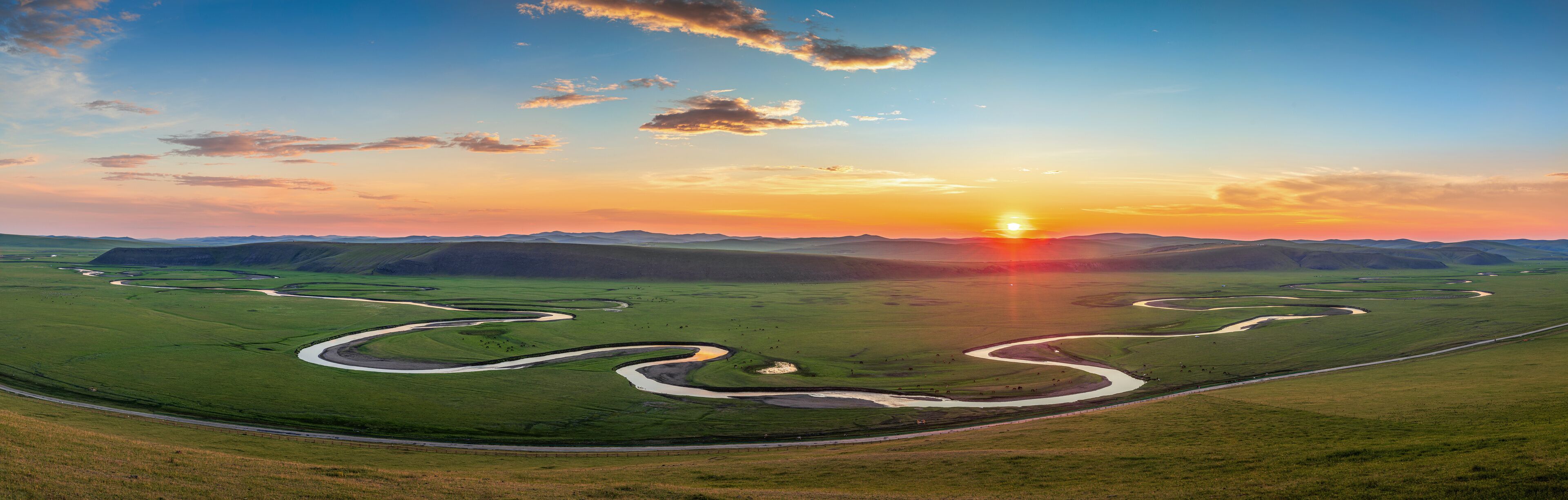 A vast green landscape with winding rivers and a sunset over rolling hills.