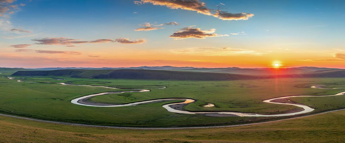 A vast green landscape with winding rivers and a sunset over rolling hills.