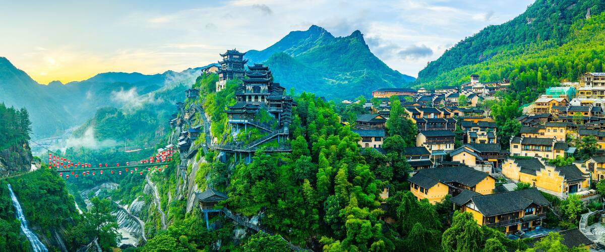 A mountainous village with traditional architecture, a waterfall, and a suspension bridge.