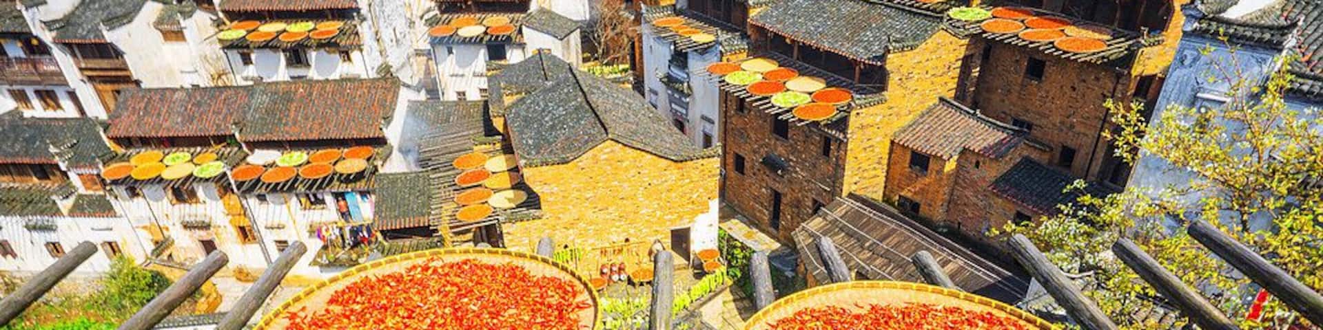 A traditional village with tiered houses and three large wooden trays filled with dried goods.