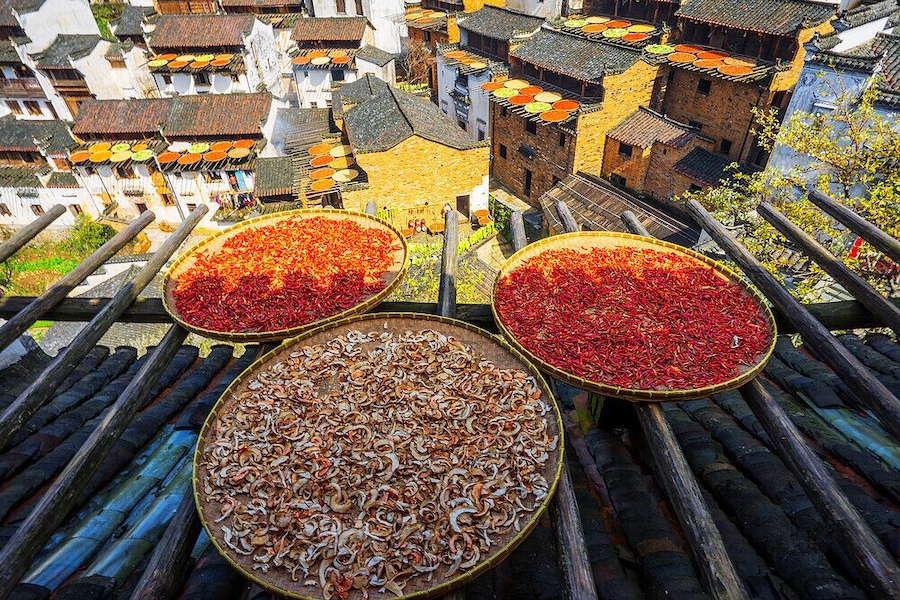 Un pueblo tradicional con casas escalonadas y tres grandes bandejas de madera llenas de productos secos.