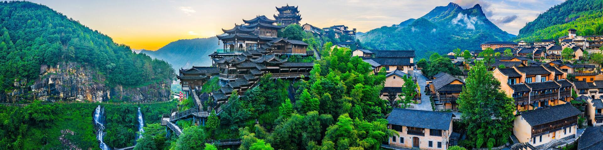 A traditional Chinese village with tiered buildings, lush greenery, and a waterfall.