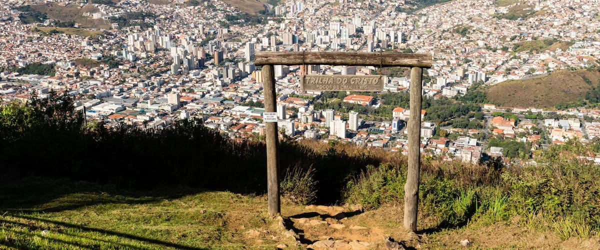 A panoramic view of a city with a signpost indicating 'TALHA DO CRISTO' and 'Focos de Caldas.'