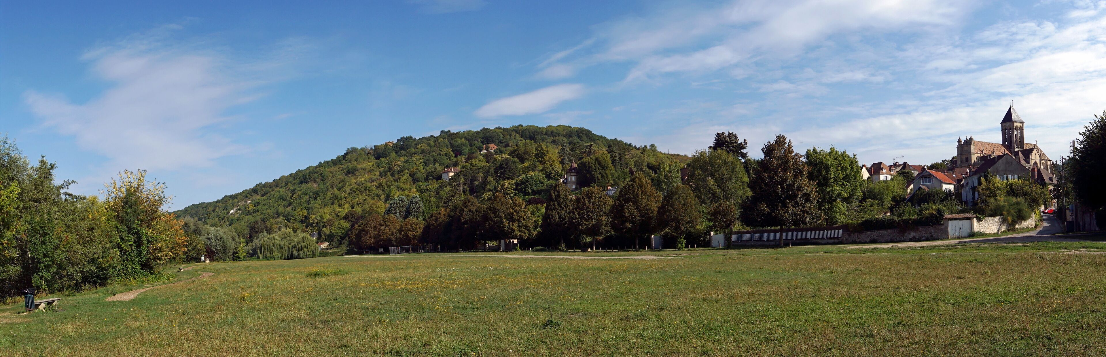 A grassy field, a hill with trees, and a church with a bell tower.
