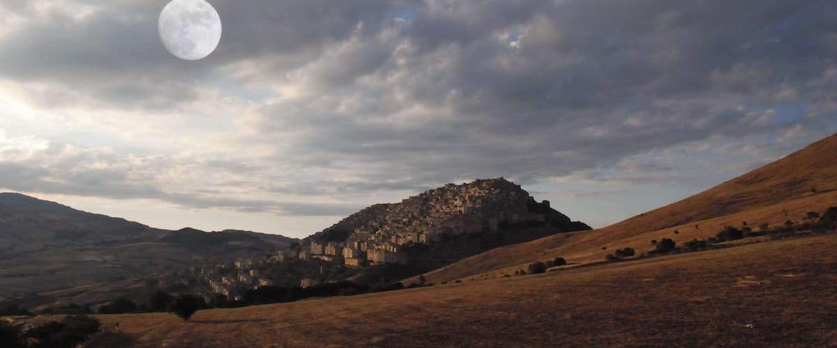 A moonlit landscape with a hilltop settlement and rolling hills.
