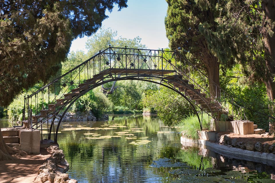 A stone bridge over a calm river, surrounded by lush greenery and trees.