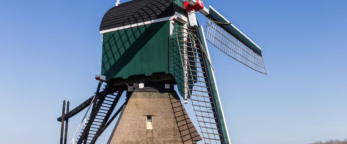 A traditional windmill with a green roof and white walls, surrounded by a wooden fence and a pathway.