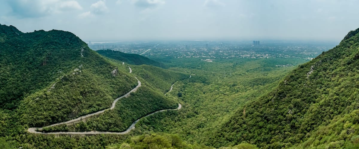 A winding road through a lush valley with steep hills on either side.