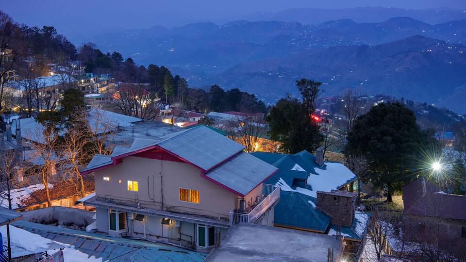 A snow-covered village with houses, a mountain range in the background, and a clear night sky.