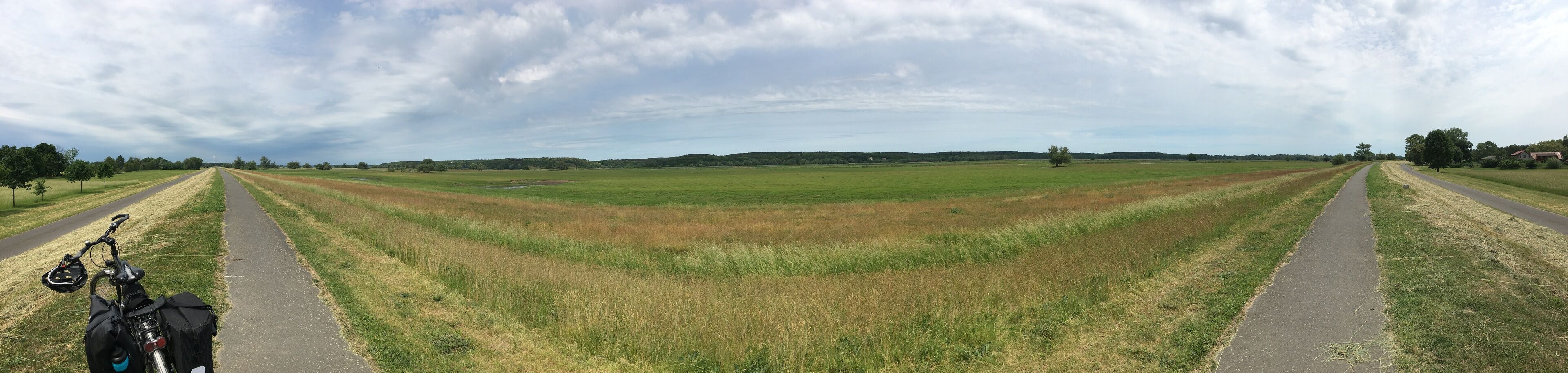 A rural landscape with a paved path splitting the field, a bicycle, and a helmet on the left.