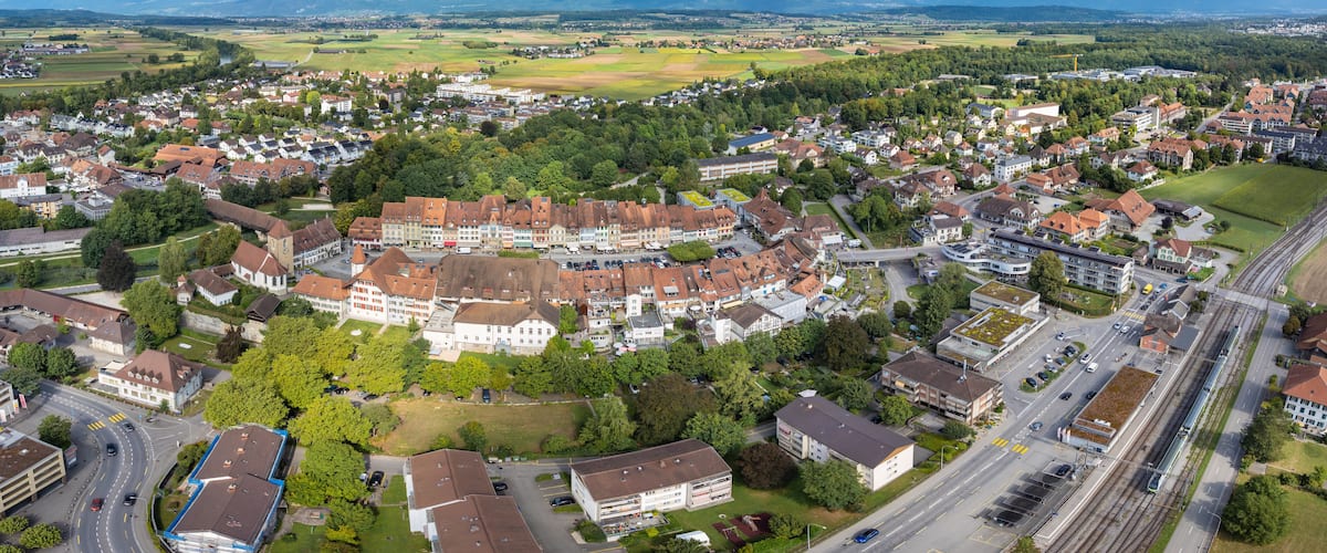 An aerial view of a town with a central roundabout, surrounded by residential buildings and green spaces.