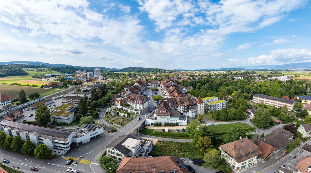 Aerial view of the old town's terracotta roofs and the expansive green fields meet under a vast blue sky, Aarberg, Canton of Bern, Switzerland.