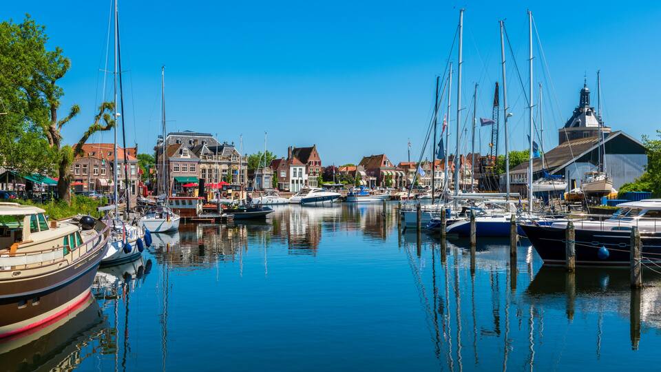 A marina with various boats docked, surrounded by historic buildings and a clear blue sky.