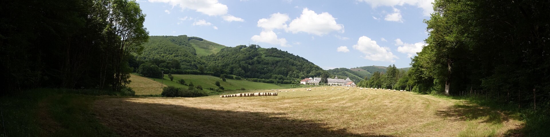 Paisagem rural com colinas onduladas, uma casa de campo e um campo cercado.