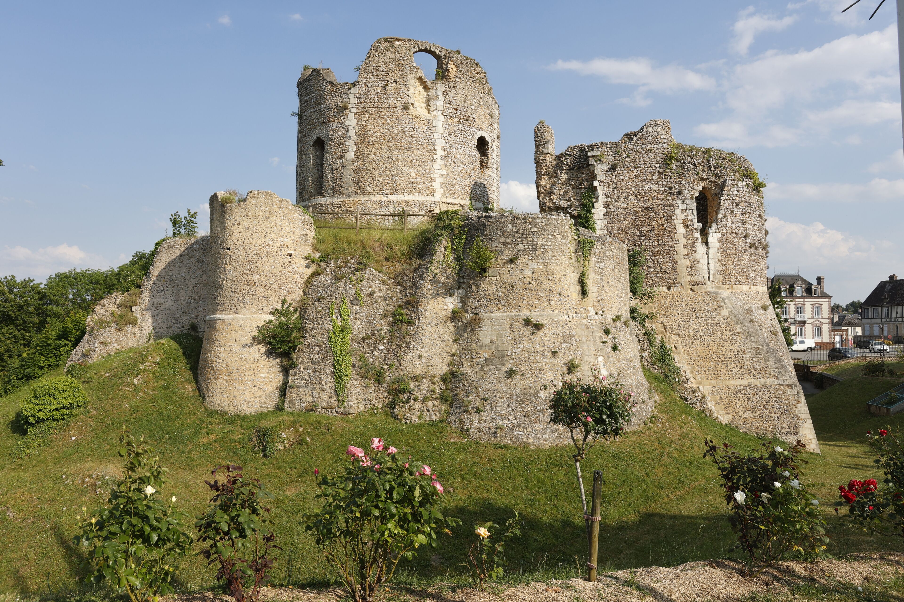 A historic stone castle with ruins, surrounded by greenery and a clear sky.