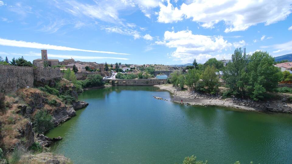 A river with a stone bridge, a castle, and a church in the background.