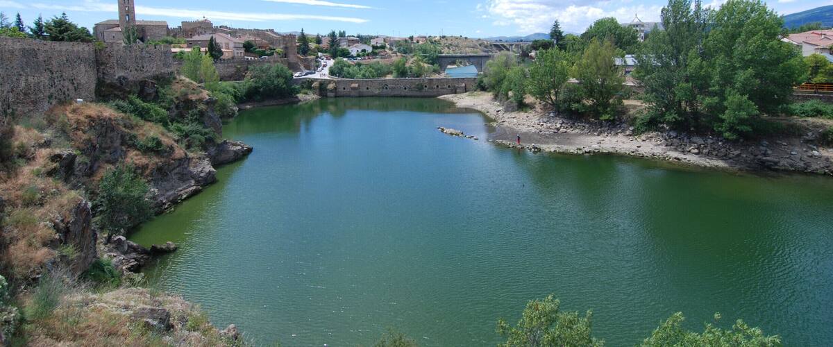 A river with a stone bridge, a castle, and a church in the background.