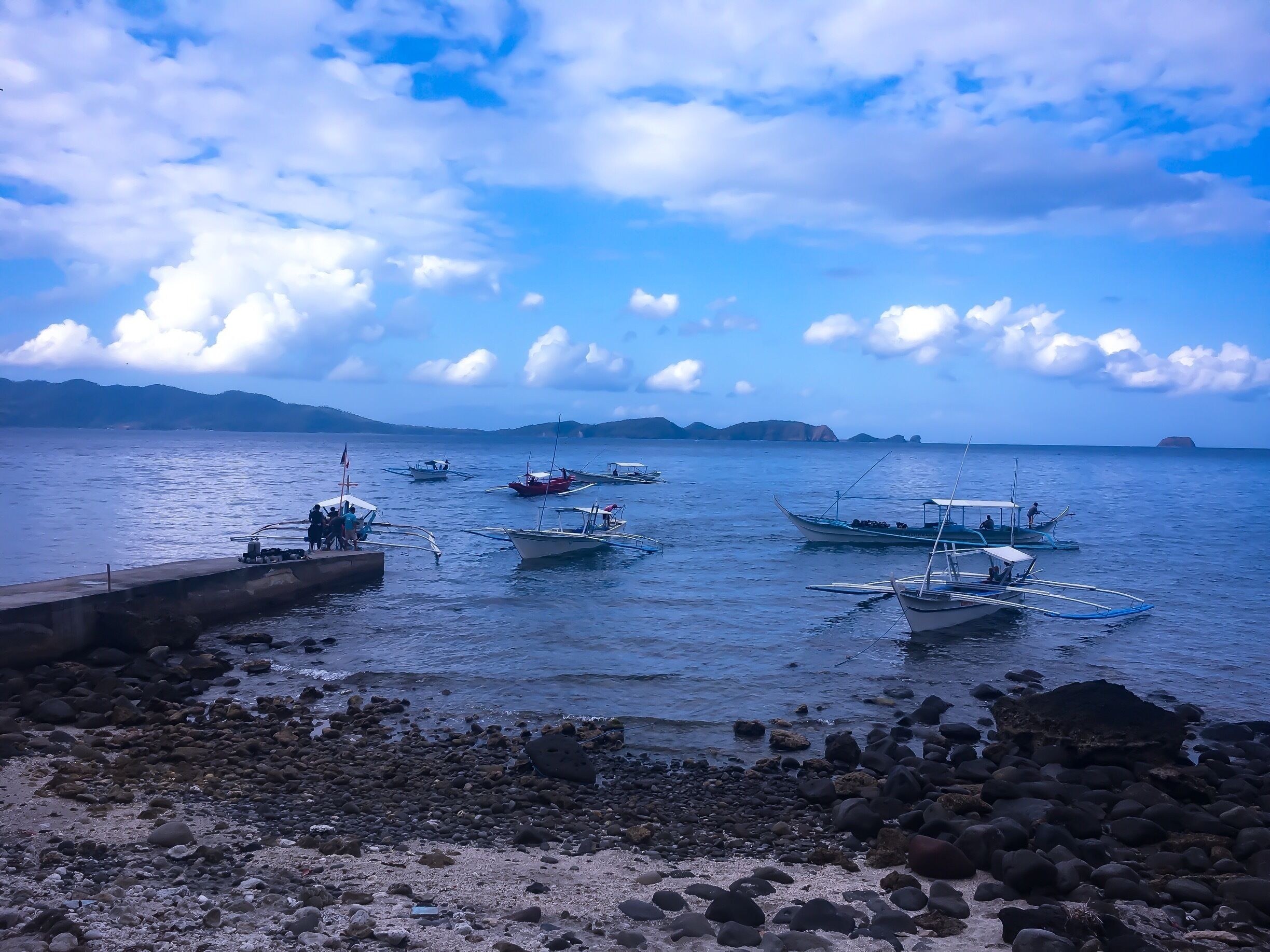 A calm sea with several boats anchored near a rocky shore.