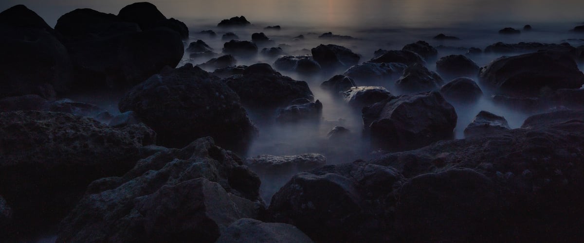 A sunset over a calm sea with rocky shores and a distant boat.