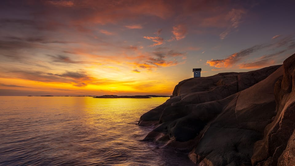 A sunset over a rocky coastline with a lighthouse on a cliff.