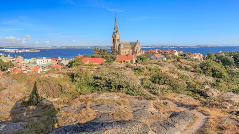 A coastal town with a prominent church on a hill, houses with red roofs, and a clear blue sky.