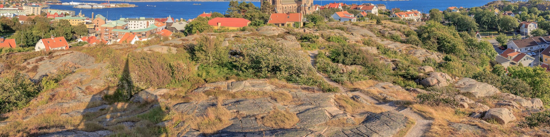 A coastal town with a prominent church on a hill, houses with red roofs, and a clear blue sky.