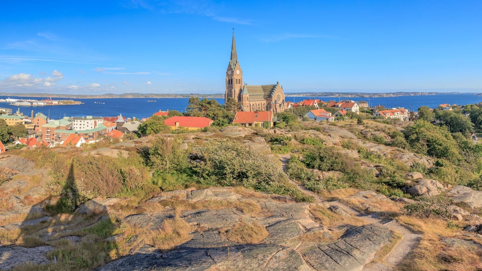 A coastal town with a prominent church on a hill, houses with red roofs, and a clear blue sky.