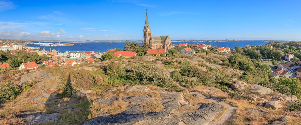 A coastal town with a prominent church on a hill, houses with red roofs, and a clear blue sky.