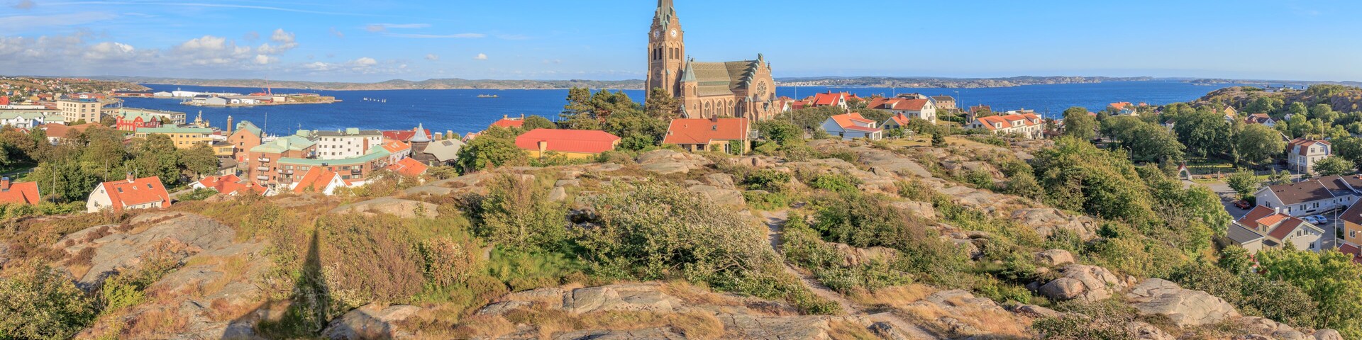 A coastal town with a prominent church on a hill, houses with red roofs, and a clear blue sky.
