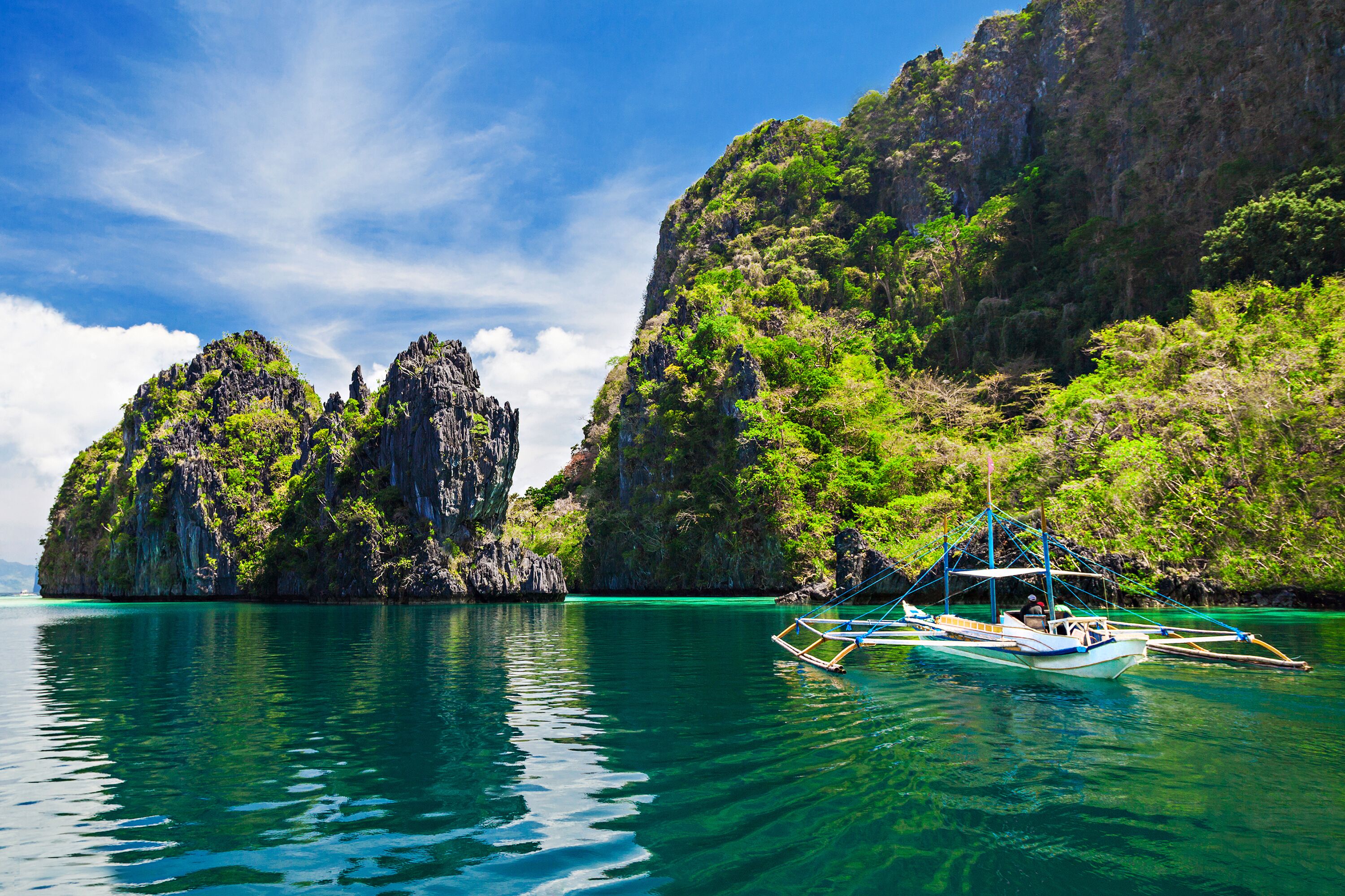 A clear turquoise sea with a traditional boat anchored near a rocky island with lush greenery.