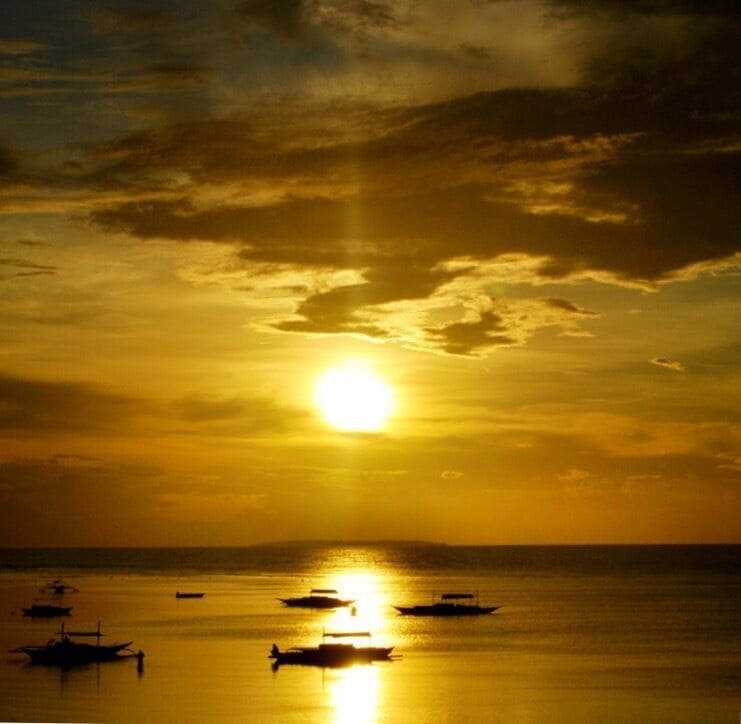 A sunset over a calm sea with several boats.