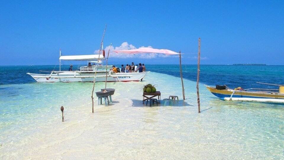 A beach with clear turquoise water, a white boat with people on board, and a smaller yellow boat anchored nearby.
