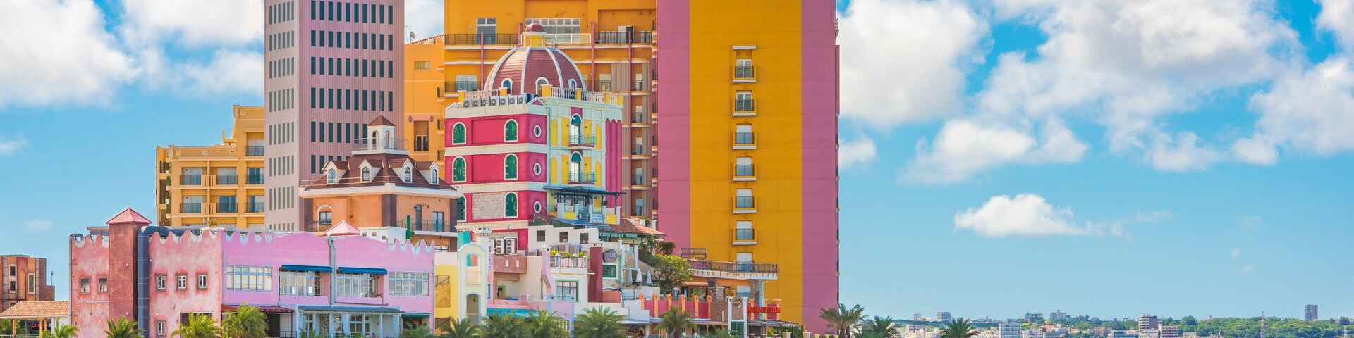 Un paisaje urbano costero con edificios coloridos, un rompeolas rocoso y un cielo azul despejado.