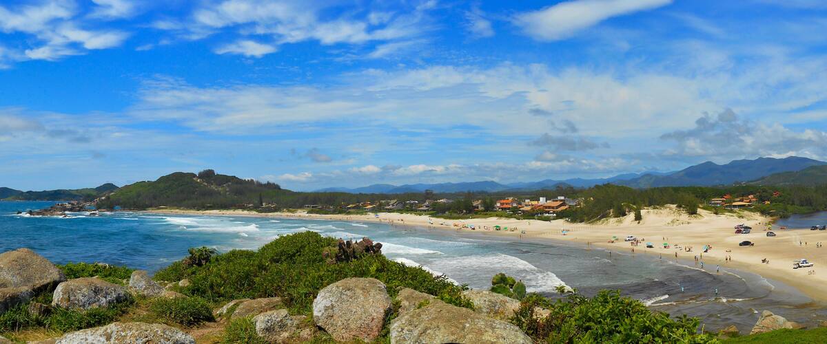 A coastal landscape with a sandy beach, rocky outcrops, and a backdrop of mountains.