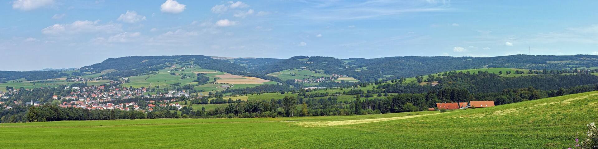 A green valley with a small town nestled among rolling hills and forests.