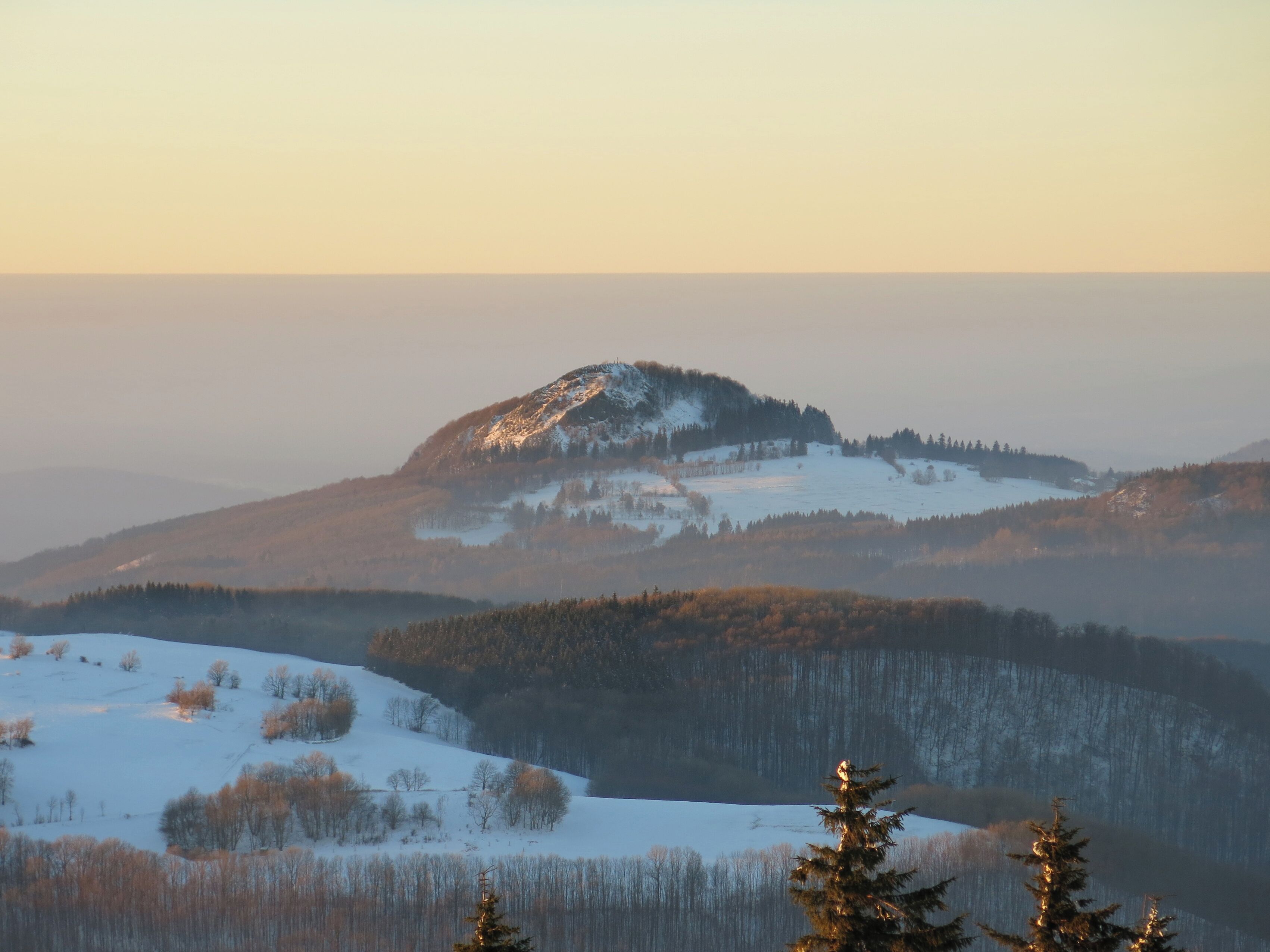 A snow-covered mountain range with a forested valley and a clear sky.