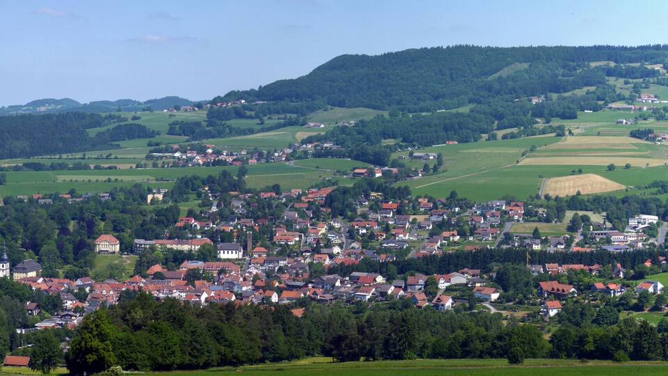 A rural town nestled in rolling hills with fields and scattered houses.