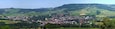 Une petite ville rurale nichée au creux de collines verdoyantes, entourée de champs et de maisons éparses.